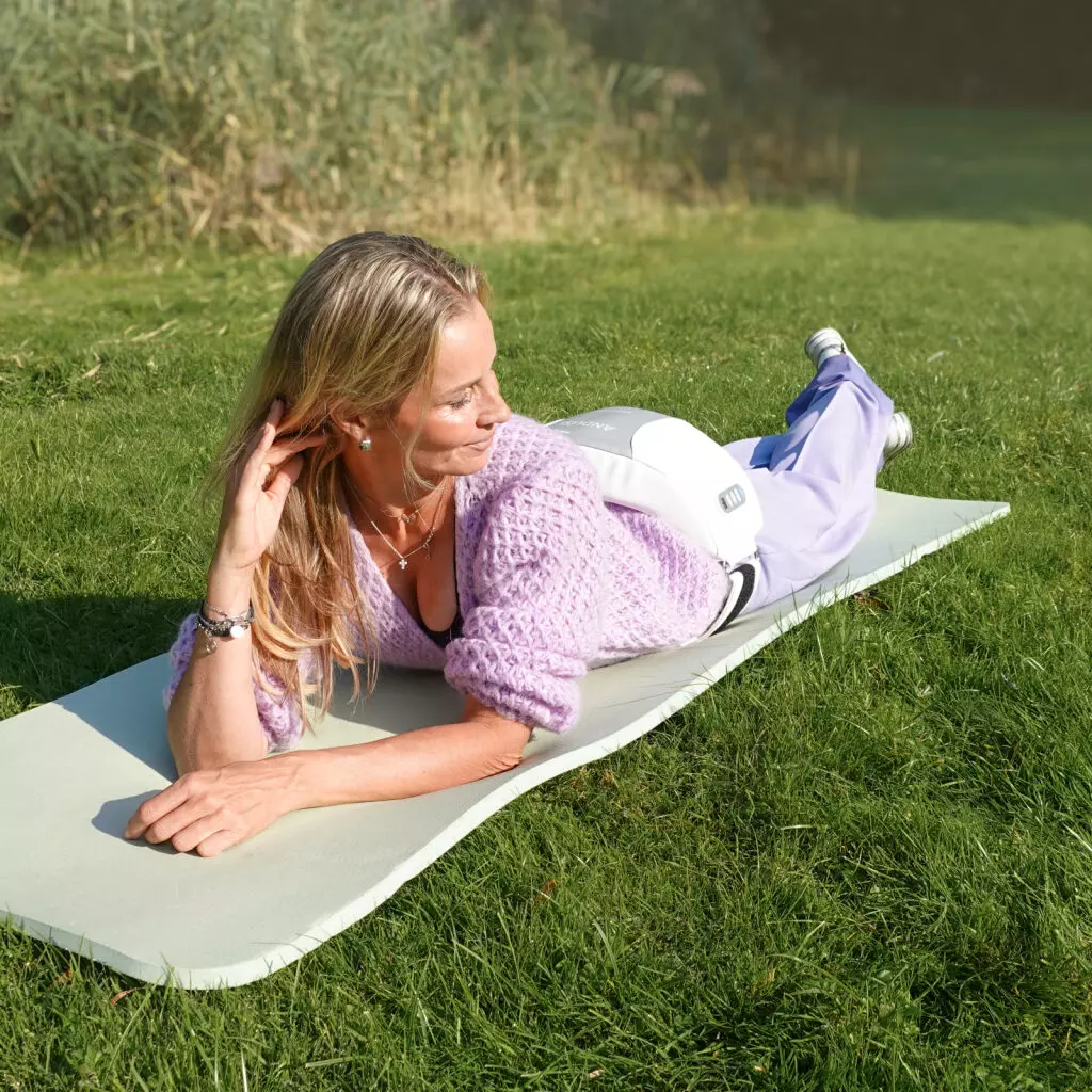 Anduslim_Andullation_Schmerztherapie_Bauchgurt_Massage_Ruecken, Yogamatte, Fitnessmatte, Liegeposition, lilafarbenePullover, Sportausrüstung